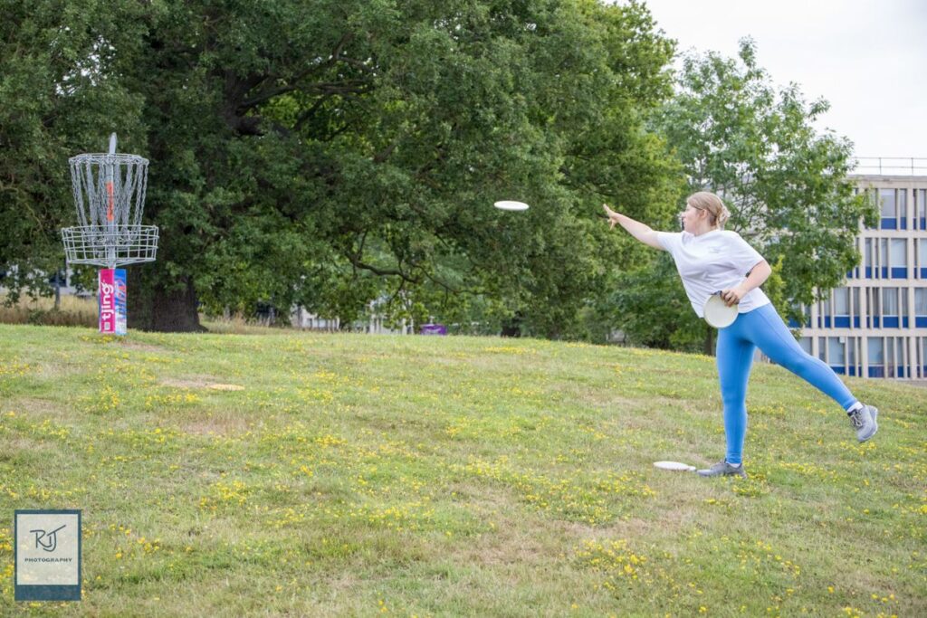 Woman putting disc golf disc into a galvanised disc golf basket.
