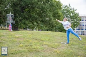 Woman putting disc golf disc into a galvanised disc golf basket.